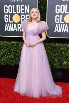 a woman in a purple gown standing on a red carpet with her hands behind her back