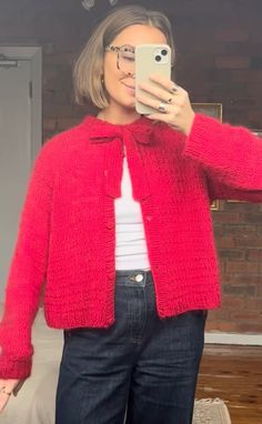 a woman taking a selfie while wearing a red cardigan sweater and black jeans