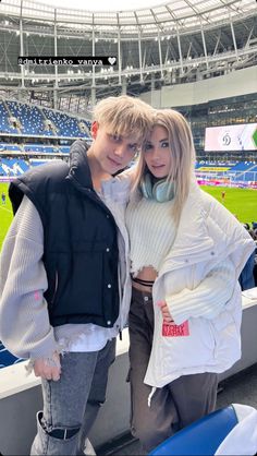 a man and woman standing next to each other in front of a soccer stadium with fans