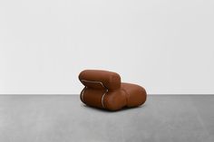 two brown leather chairs sitting next to each other on top of a cement floor in front of a white wall