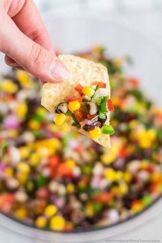 a hand holding a tortilla chip over a bowl of mexican salad