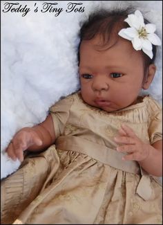 a baby wearing a gold dress with a flower in it's hair sitting on a blanket