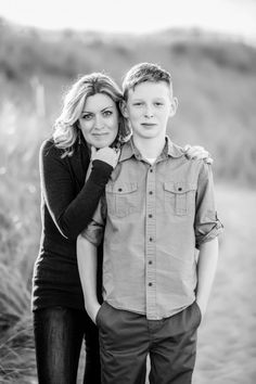 a young man and woman standing next to each other in front of tall grass with the sun shining on them