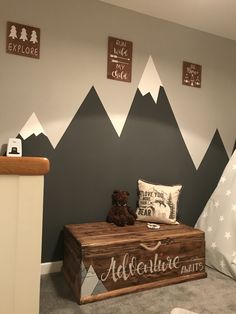 a child's room with mountains painted on the wall and a teddy bear sitting on a trunk