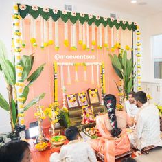 a group of people sitting in front of a wall decorated with flowers and garlands