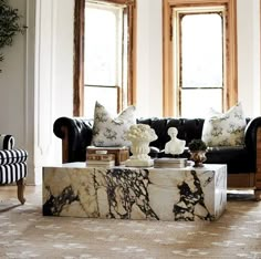 a living room with black couches and marble coffee table in front of two windows