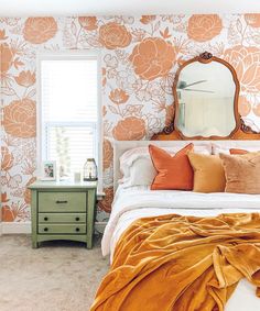 a bedroom with floral wallpaper and orange bedding, mirror on the side table