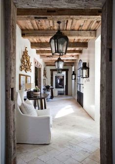 an open door leading to a living room with white furniture and wood beams on the ceiling