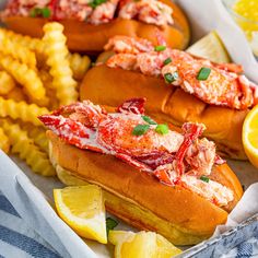 two lobster sandwiches and french fries in a tray with lemon wedges on the side