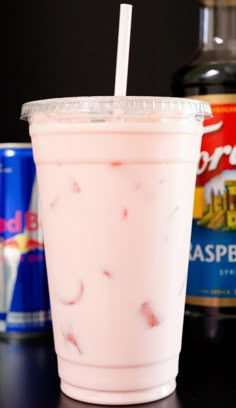 a pink drink with a straw in it sitting on a table next to cans of soda