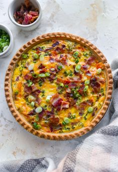 a quiche with bacon and green onions in a pie pan next to bowls of salad