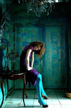 a woman sitting on top of a chair in front of a table with a chandelier