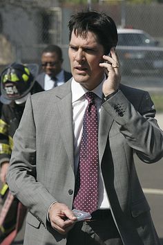 a man in a suit and tie talking on a cell phone while standing next to fire fighters