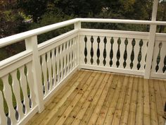 a deck with white railings and wood flooring in front of some green trees