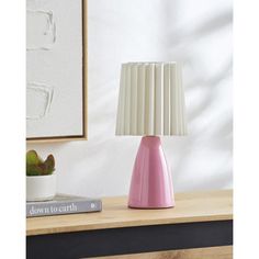 a pink lamp sitting on top of a table next to a book and potted plant