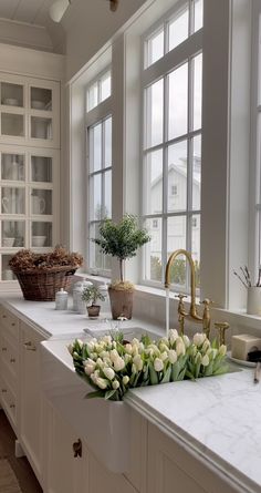 a kitchen with white cabinets and marble countertops has flowers in the window sill