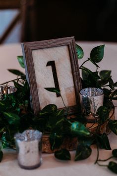 the table is set with candles and an old photo frame on top of some greenery