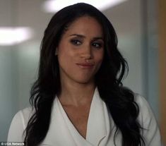 a woman with long black hair wearing a white shirt and looking at the camera while standing in front of a mirror