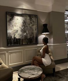 a woman sitting on a chair in a living room next to a table and lamp