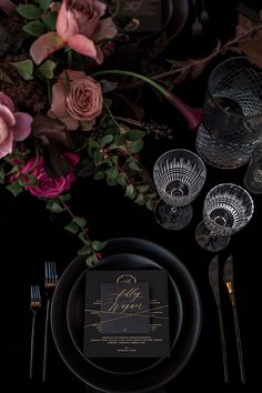 the table is set with black plates, silverware and pink flowers in vases