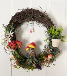 a wreath with mushrooms, flowers and plants hanging on the wall next to a potted plant