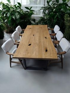 a large wooden table surrounded by white chairs and potted plants in an office setting