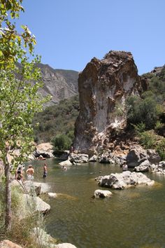 people are wading in the water near large rocks