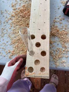 a person holding a piece of wood with holes in it and sand on the ground