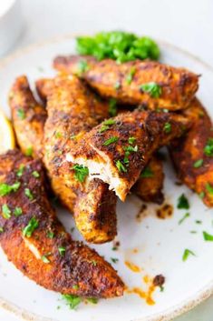 some chicken wings are on a plate with lemon wedges and garnishes