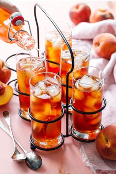 several glasses filled with liquid and ice on a table next to peaches, apples and spoons