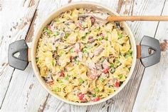 a pot filled with pasta and meat on top of a white wooden table next to two spatulas