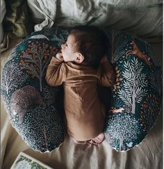 a baby laying on top of a round pillow next to a book and some pillows