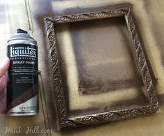 a person is holding a spray paint in front of a picture frame on a table