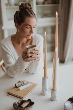 a woman sitting at a table holding a coffee cup with candles in front of her