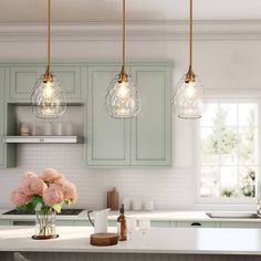 three lights hanging over a kitchen island with flowers in vases on the counter top