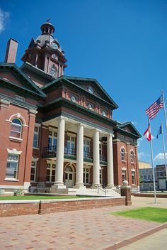 an old brick building with two flags flying in the wind and a clock tower on top