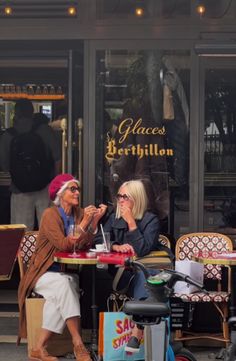 two women sitting at a table in front of a store