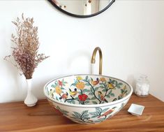 a bowl shaped sink sitting on top of a wooden counter next to a vase with flowers