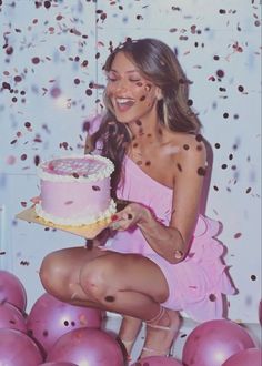 a woman holding a cake in front of balloons and confetti on the wall