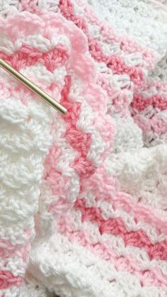 a crocheted blanket with pink and white stripes on it, next to a knitting needle