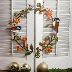 two birds on a branch with flowers and leaves in front of white shuttered doors