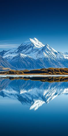 snow covered mountains reflect in the still water of a lake on a clear, sunny day