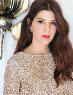 a woman with long hair standing in front of a gold flower wall hanging on the wall