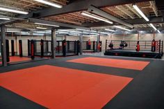 an indoor gym with red mats and black boxing gloves on the floor, surrounded by gray walls