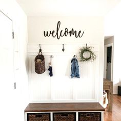 a white entryway with baskets and coat hooks on the wall next to a welcome sign