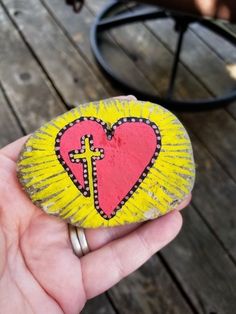 a hand holding a rock with a cross painted on it and a heart in the middle