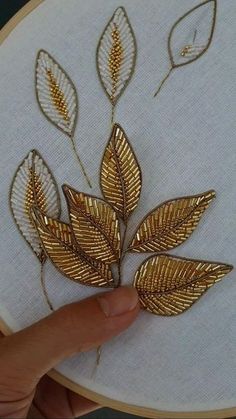 a hand is holding up a gold leaf on a white embroidery hoop that has been stitched onto it