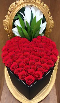 a heart shaped box filled with red roses on top of a wooden table next to a mirror