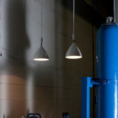 two lights hanging from the ceiling in a room with concrete walls and blue steel pipes