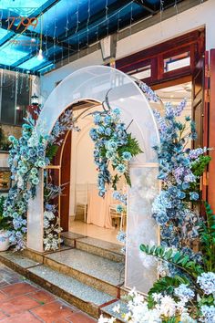 an arch with blue flowers and greenery hanging from it's sides in front of a building